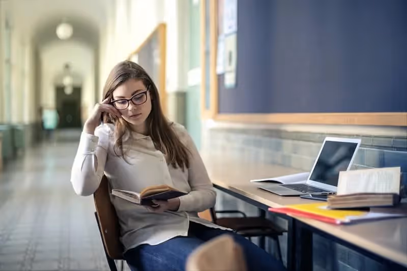 Jeune fille assise dans le couloir qui étudie et lit un livre sur le participe passé anglais