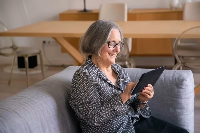 femme âgée qui traine sur son téléphone assise sur le canapé