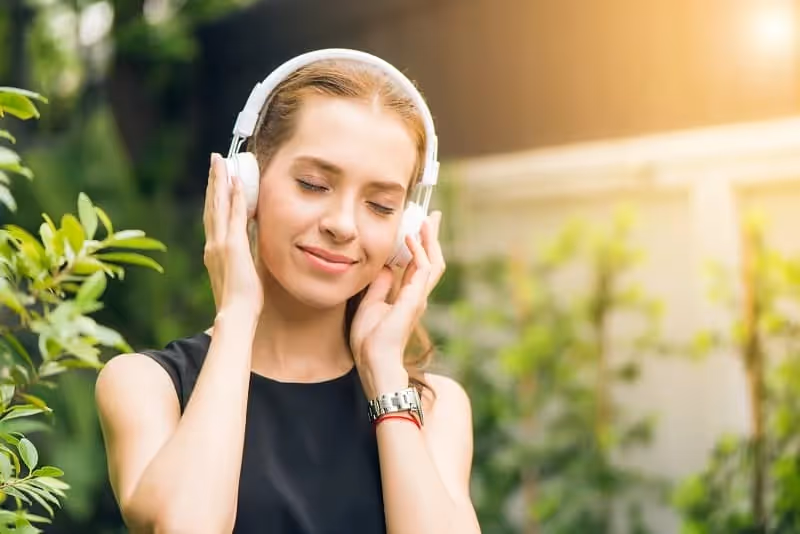 femme qui écoute de la musique avec un casque avec un fond de nature derrière elle