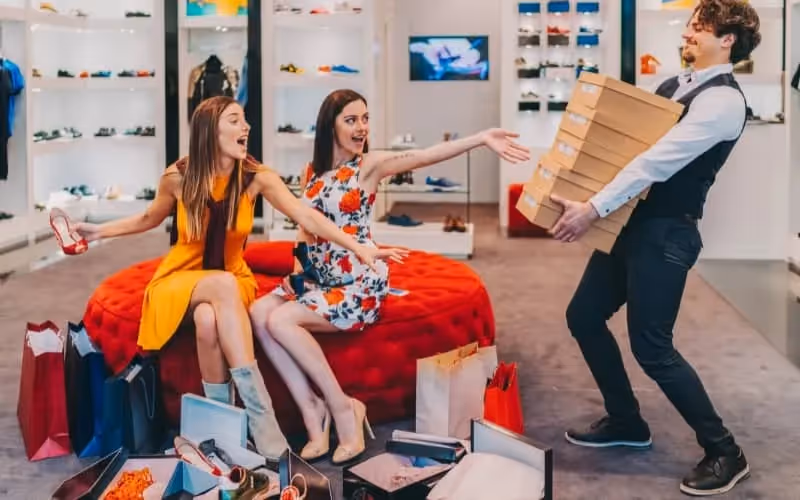 Jeunes femmes qui font du shopping et qui essaient dans un magasin plusieurs paires de chaussures pendant le black friday