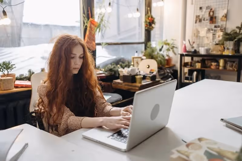 Jeune fille rousse aux cheveux longs qui est concentrée face à son ordinateur