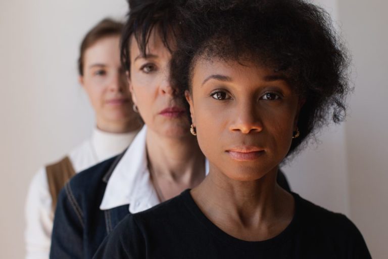 Portrait en gros plan de trois personnes debout en rang et fixant l'appareil photo sans sourire. 