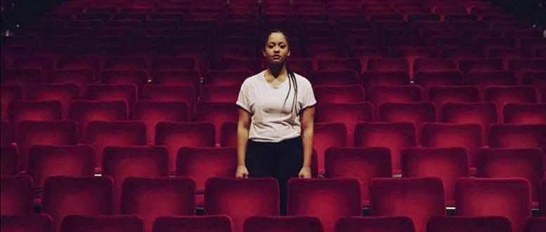 A person standing in an auditorium of empty red seats.