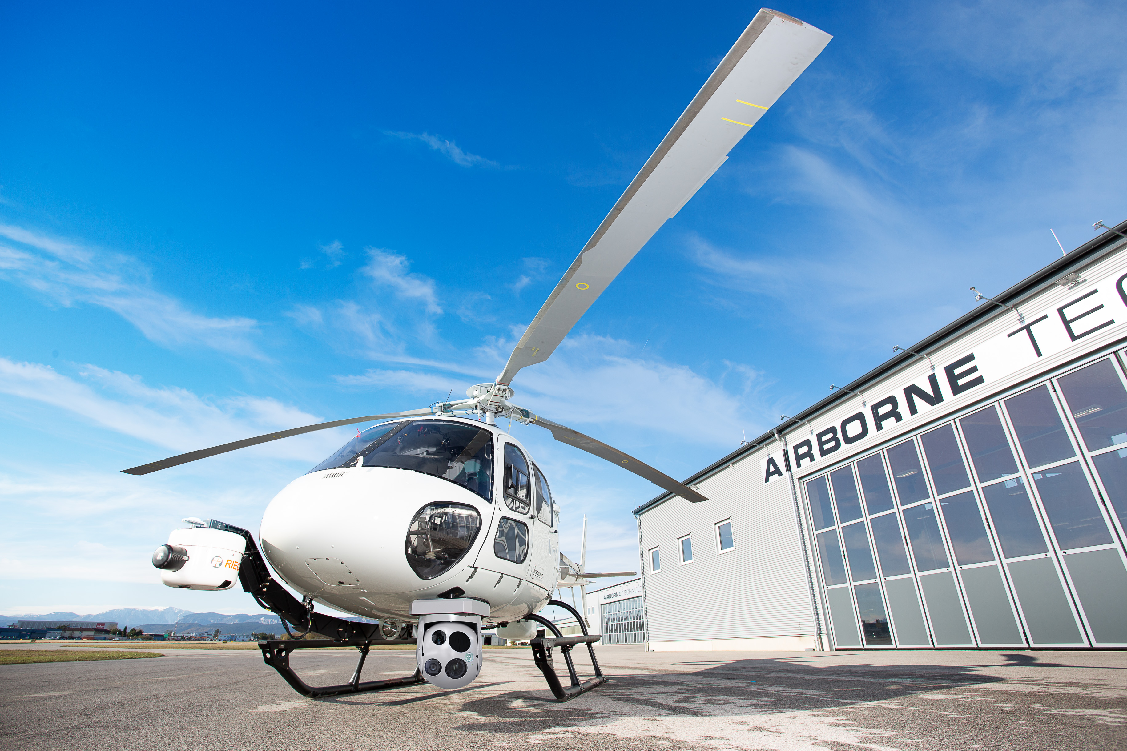 A wide angle image of a helicopter in front of the airborne technology hangar