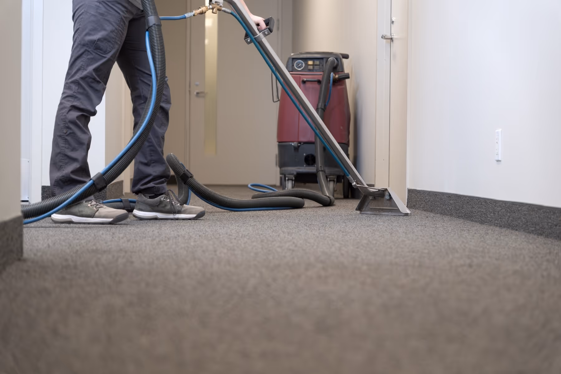Professional carpet cleaning technician using extraction equipment in hallway