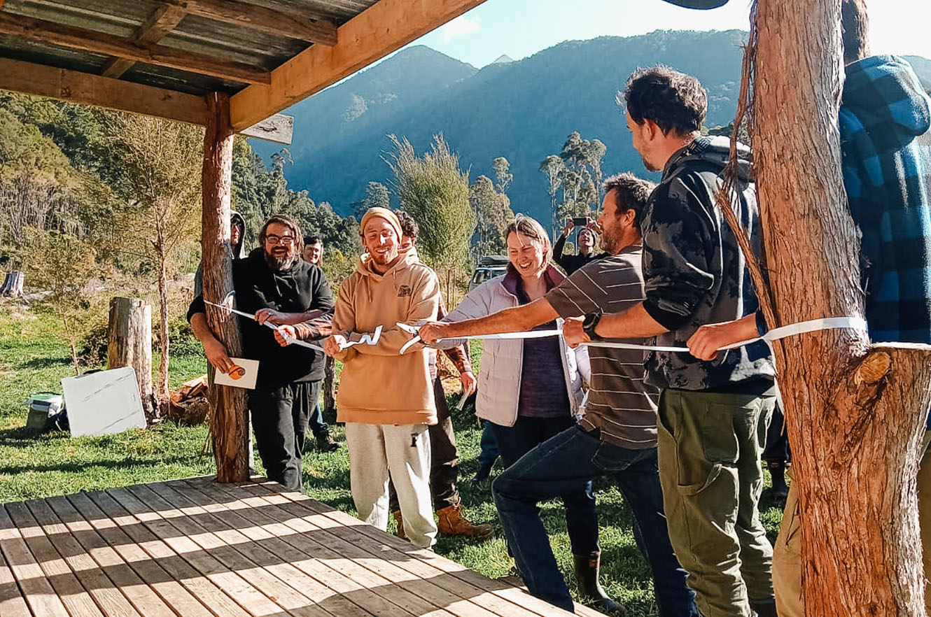 A group of people cut a white ribbon tied to a cabin