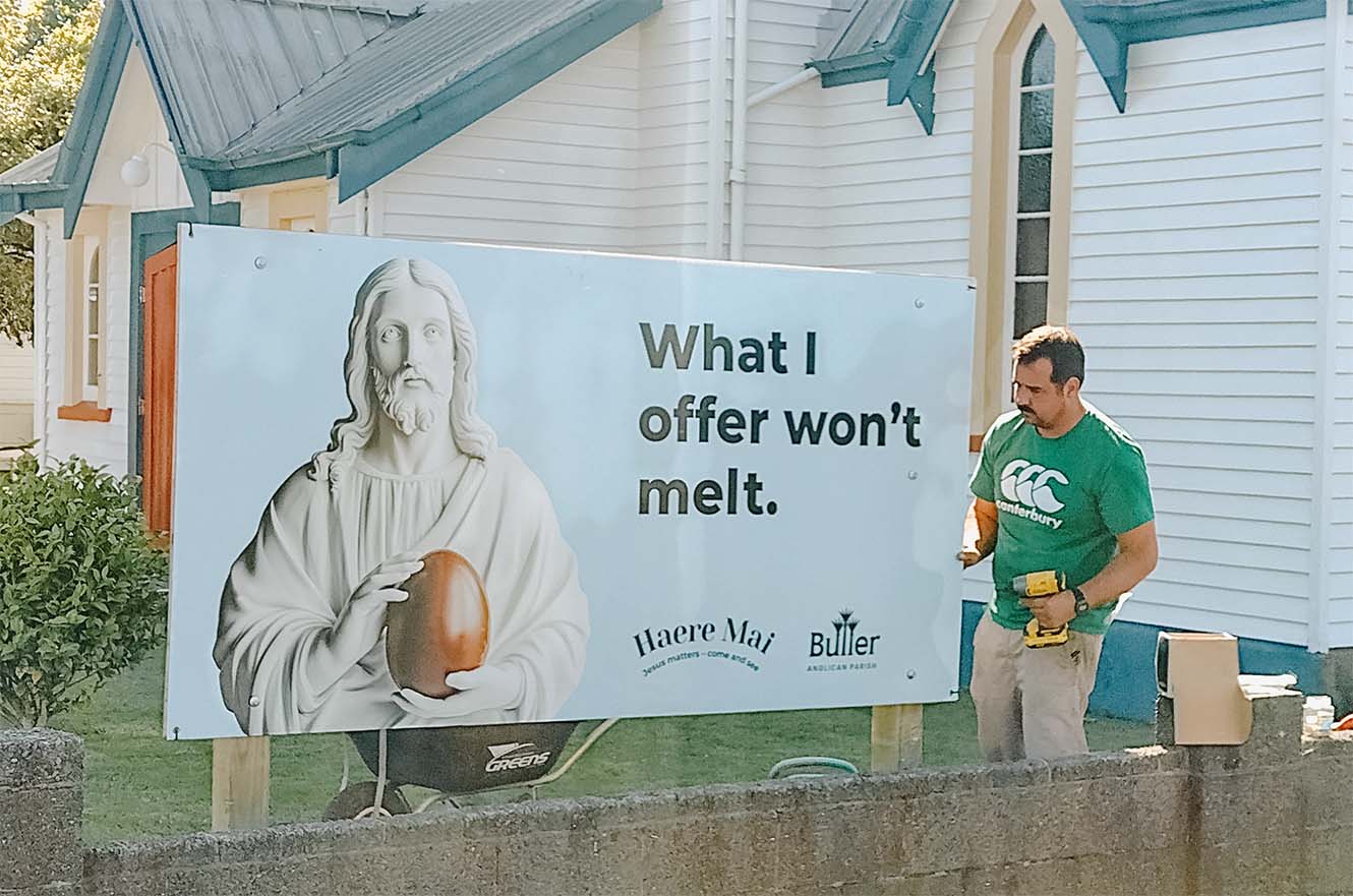 A man installs a Haere Mai billboard outside St John's in Westport