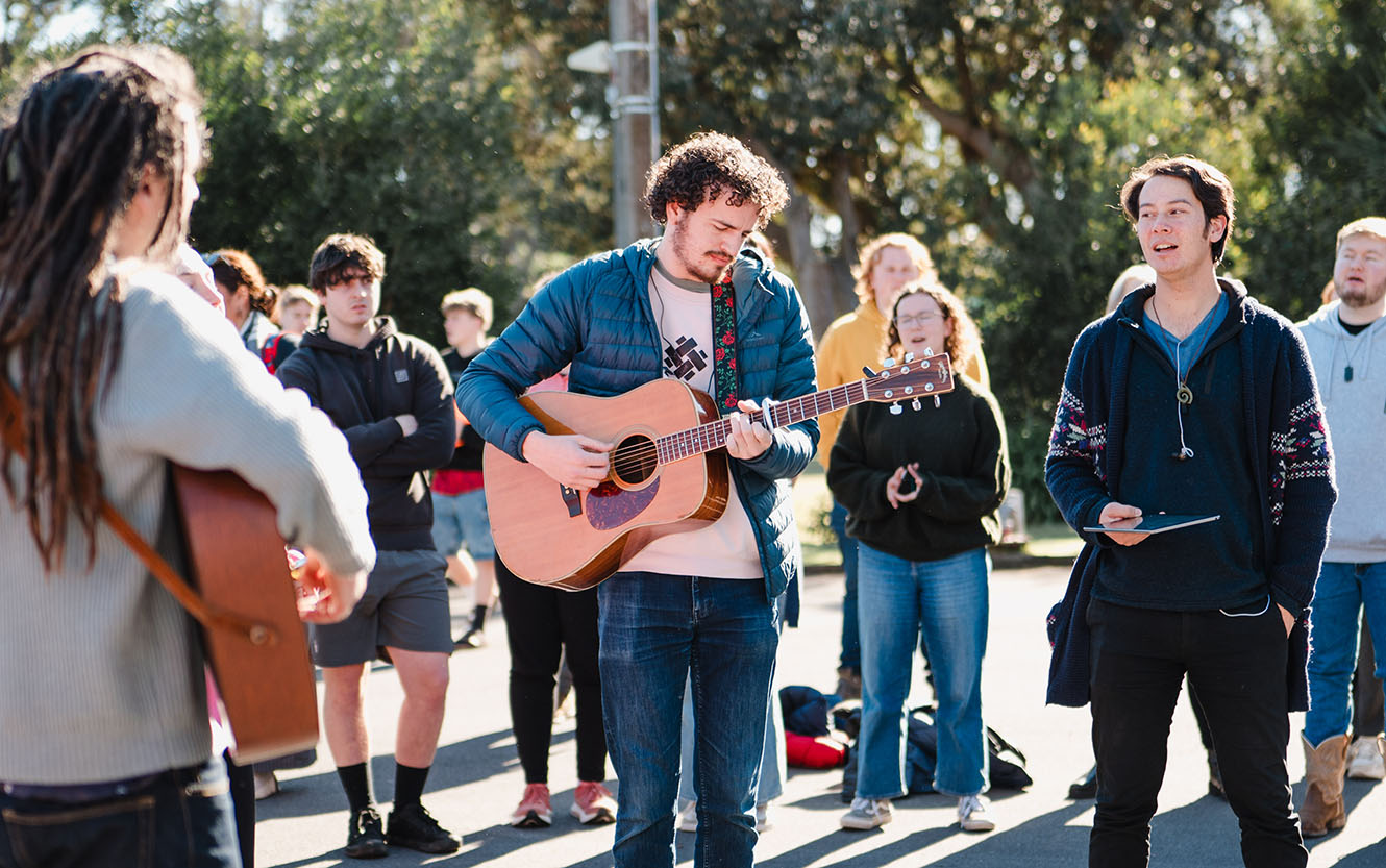Musicians play outside in the sun surrounded by a crowd