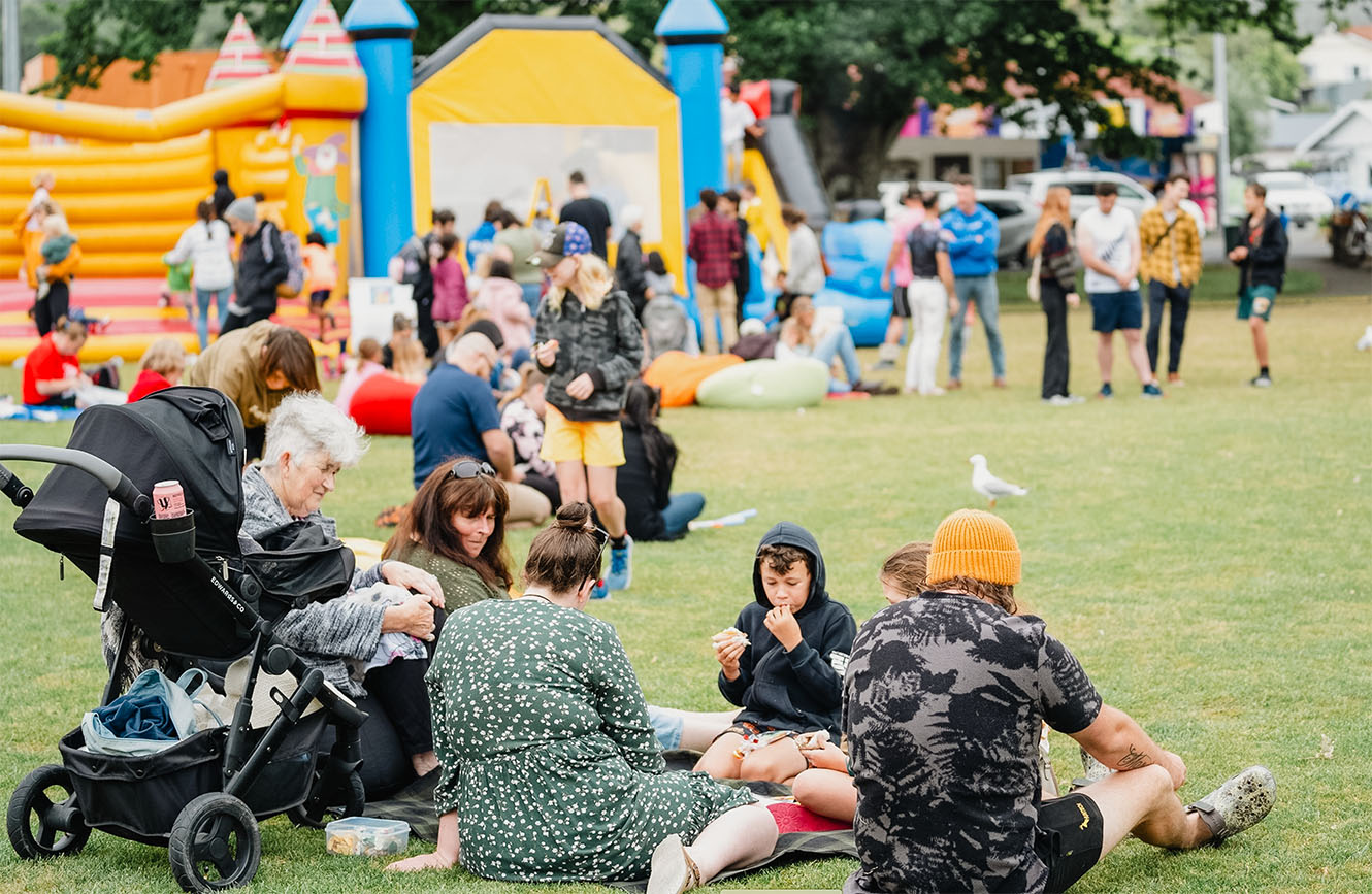 an outdoor event with people eating and a bouncy castle in the background