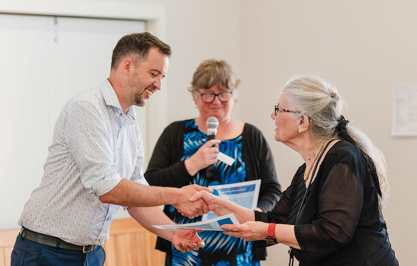 Jason Shaw, social services coordinator, shakes chaplain Jane Jensen's hand and hands over a certificate