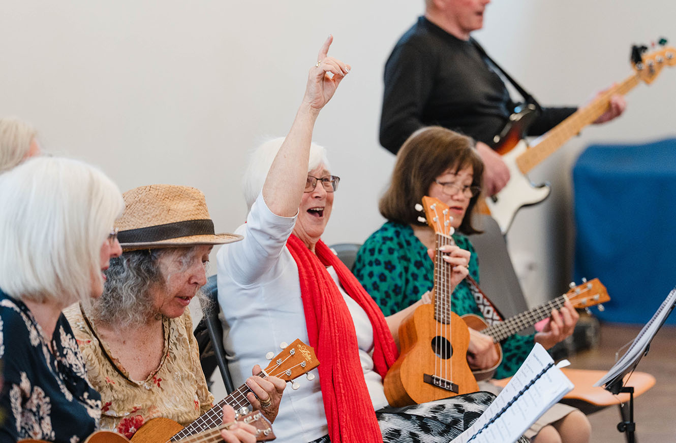 A lady raises her hand in joy as part of a band playing on ukeleles