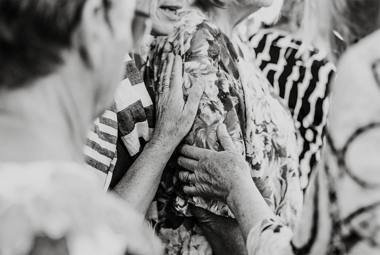 Hands being laid on a woman in prayer