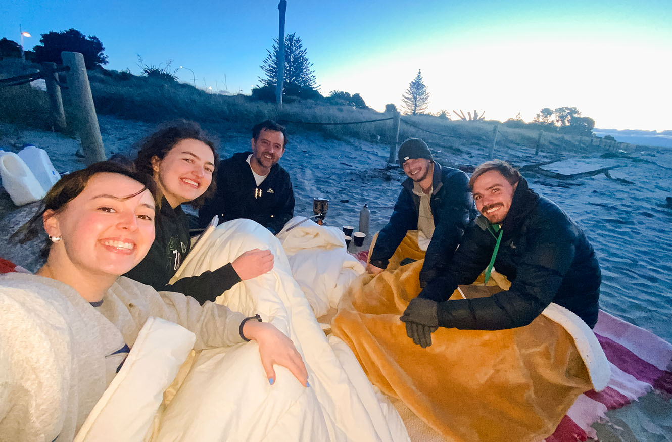 the members of Suter House share hot drinks on the beach as the sun sets