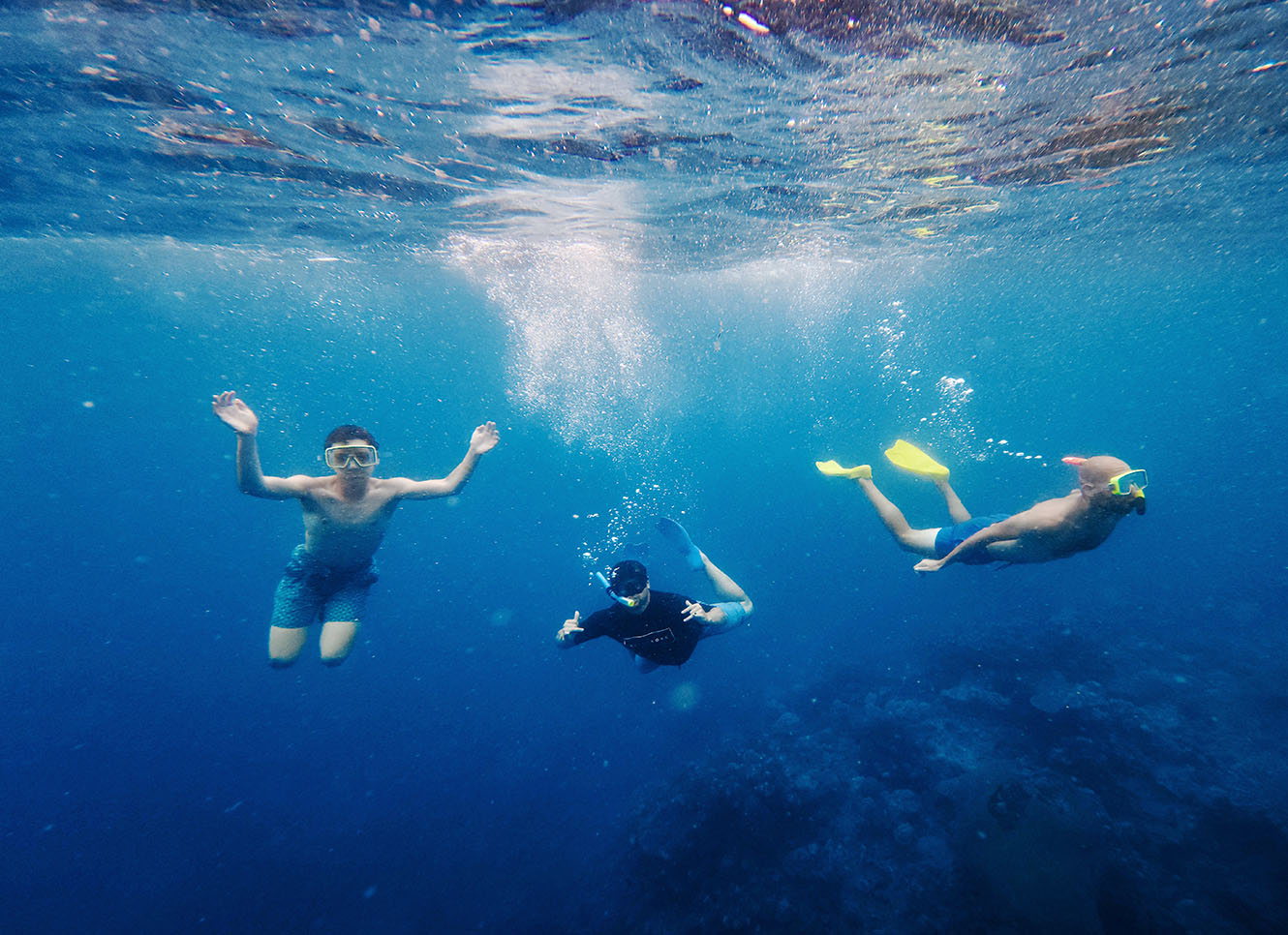 3 people snorkelling in bright blue water