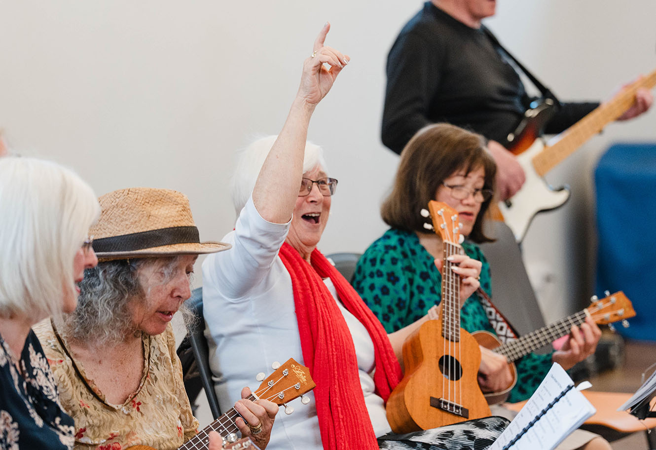 a woman raises her arm excitedly in a ukulele playing band