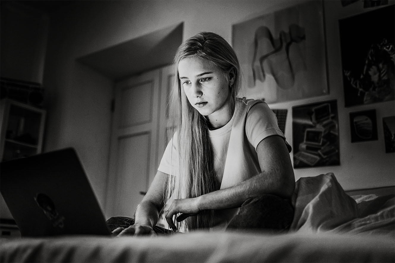 A young woman browsing on a laptop in a bedroom