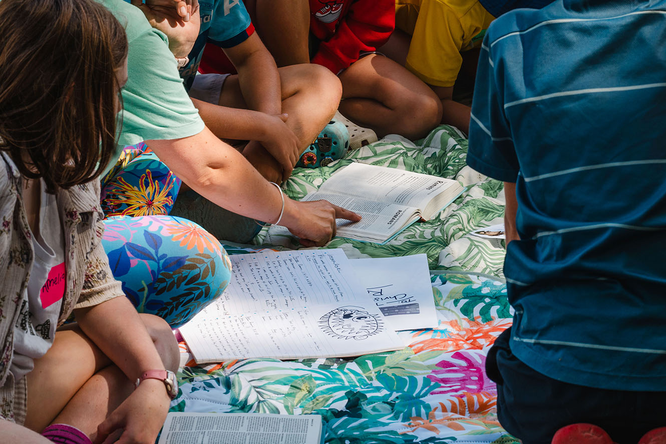 young people surround an open Bible outside in the sun