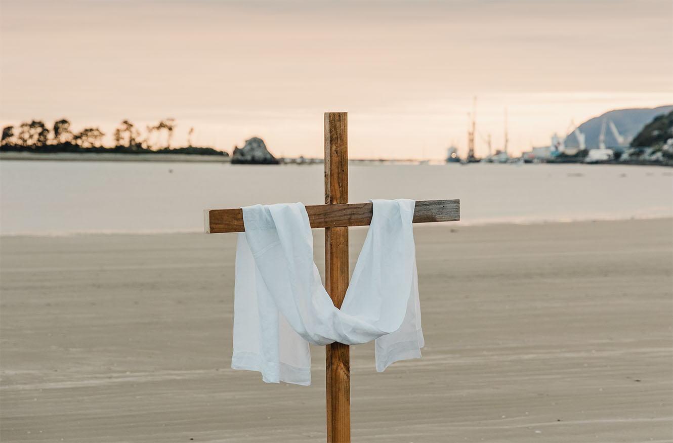 A wooden cross standing on Tahunanui Beach at sunrise.