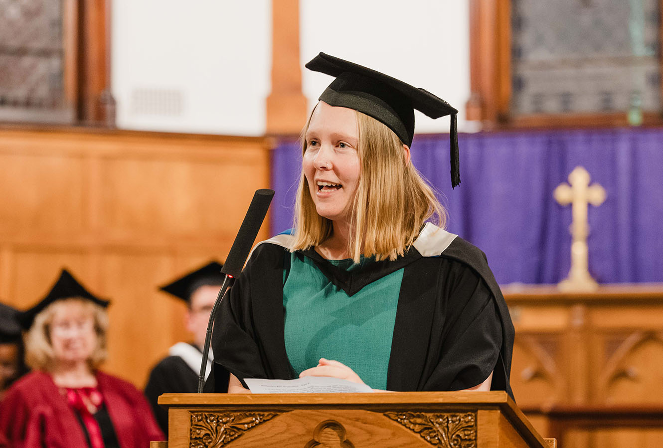 A Bishopdale student in graduation attire, speaking from a lectern.