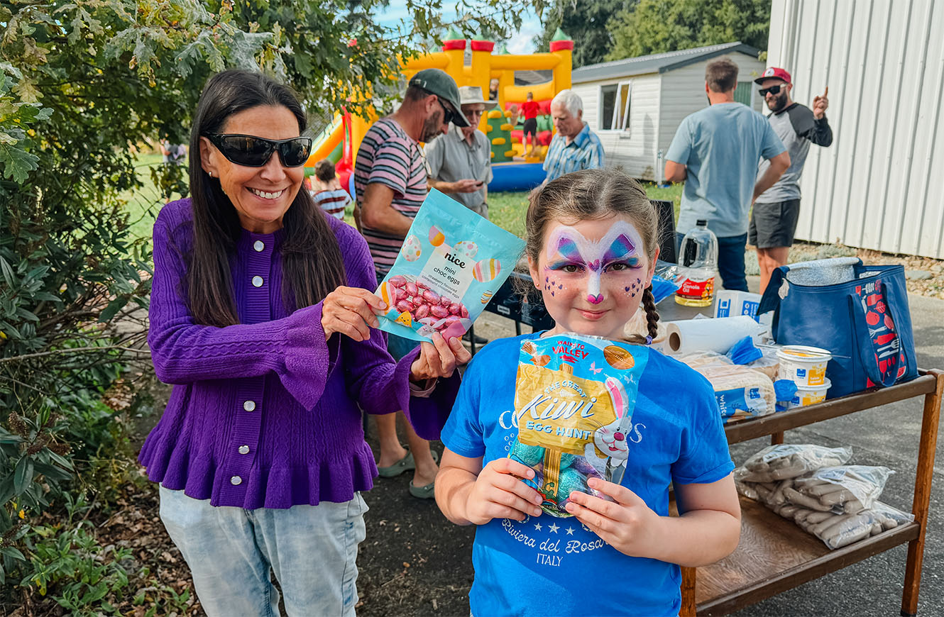 A girl and a woman hold chocolate eggs. The girl's face is painted in bright blue and purple colours.