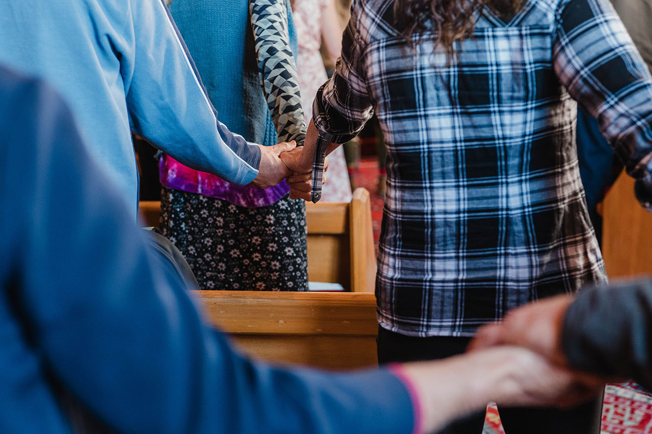 people holding hands over church pews