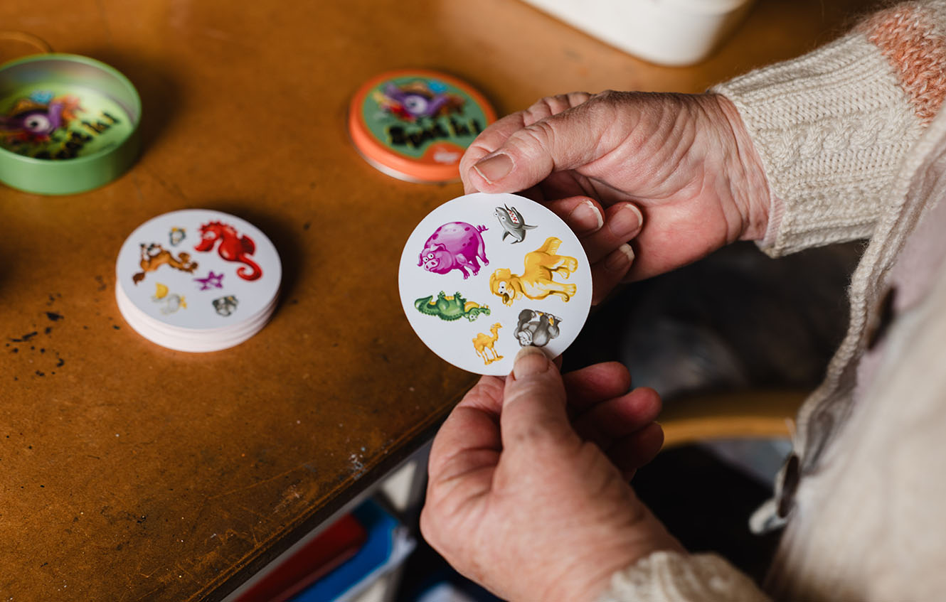 Hands holding a card from the game "Spot it" or "Dobble", showing several animal pictures
