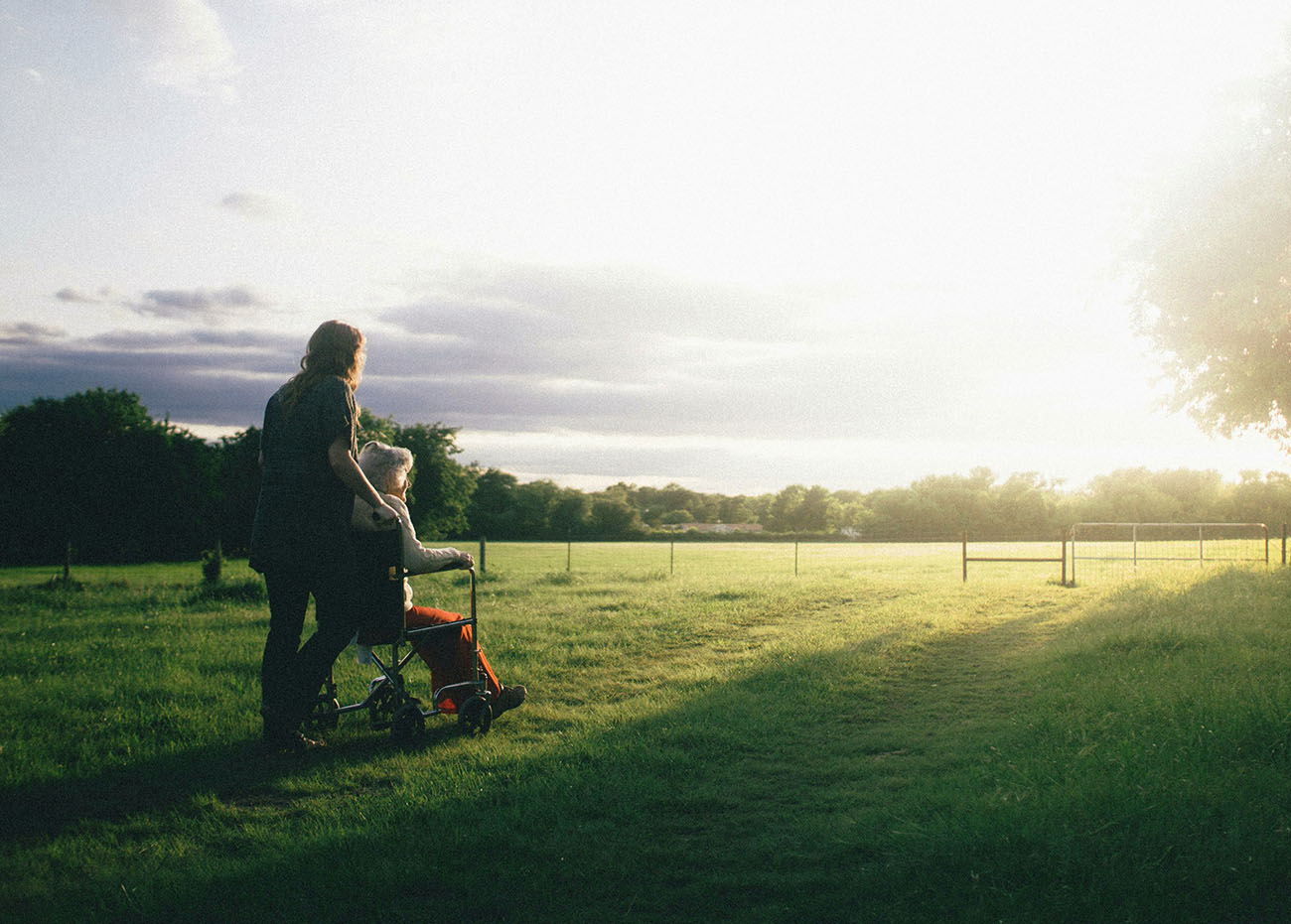 A woman pushing an elderly lady in a wheelchair outside in a meadow