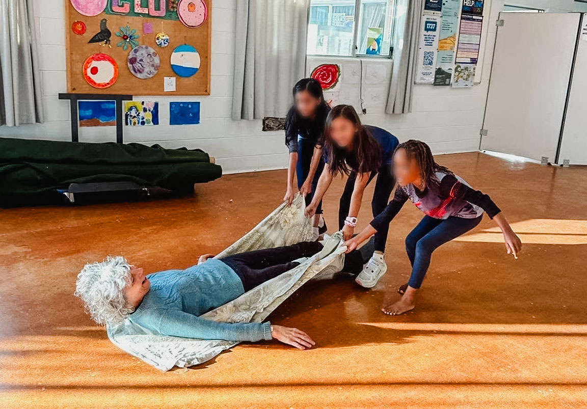 Maria is dragged across the floor on a blanket by three children
