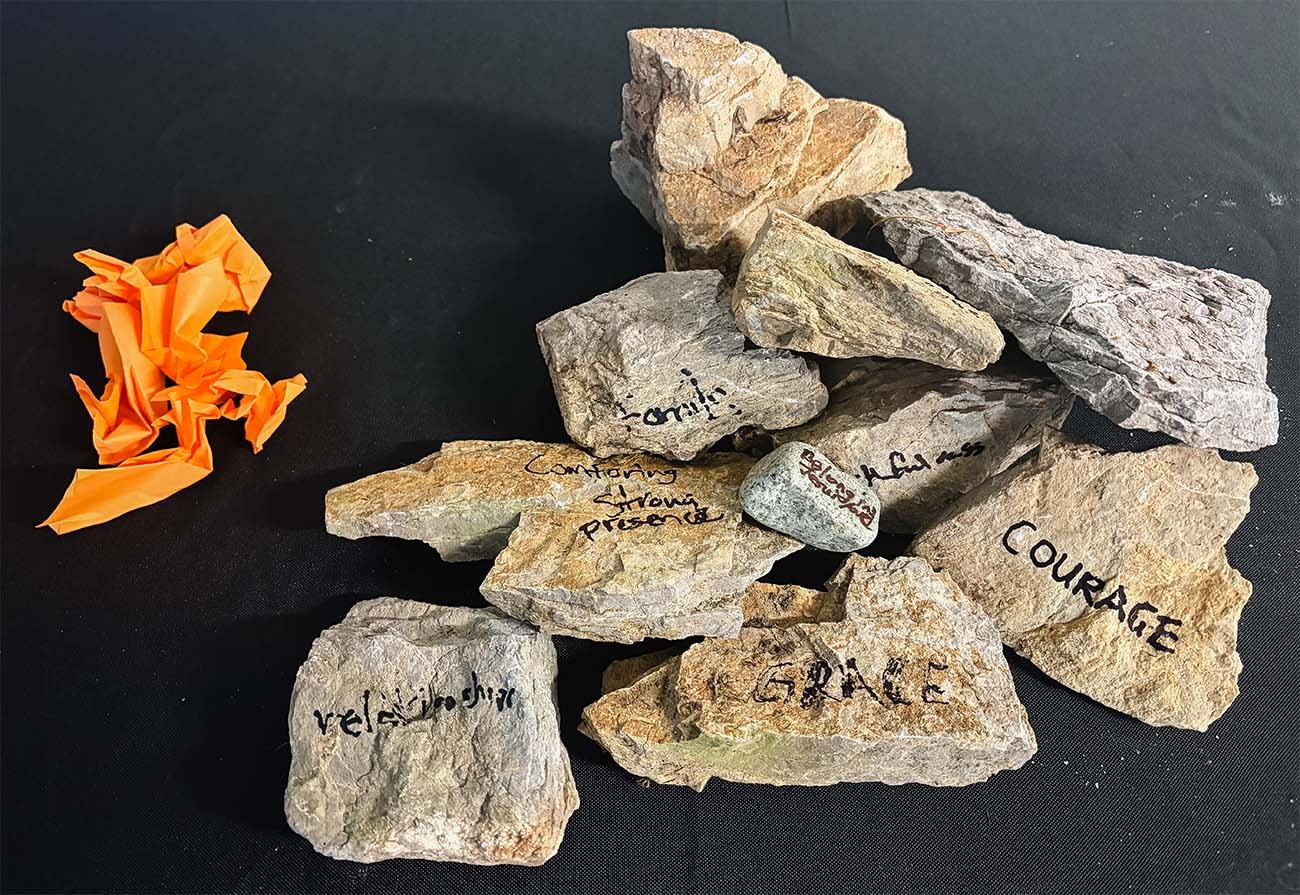 A small monument of rocks with words penned on each, next to a few pieces of crumpled paper