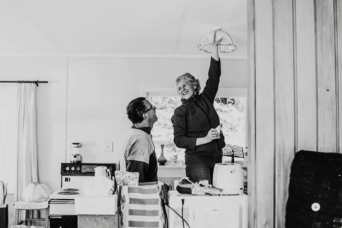 a woman changes a lightbulb, smiling at a man watching