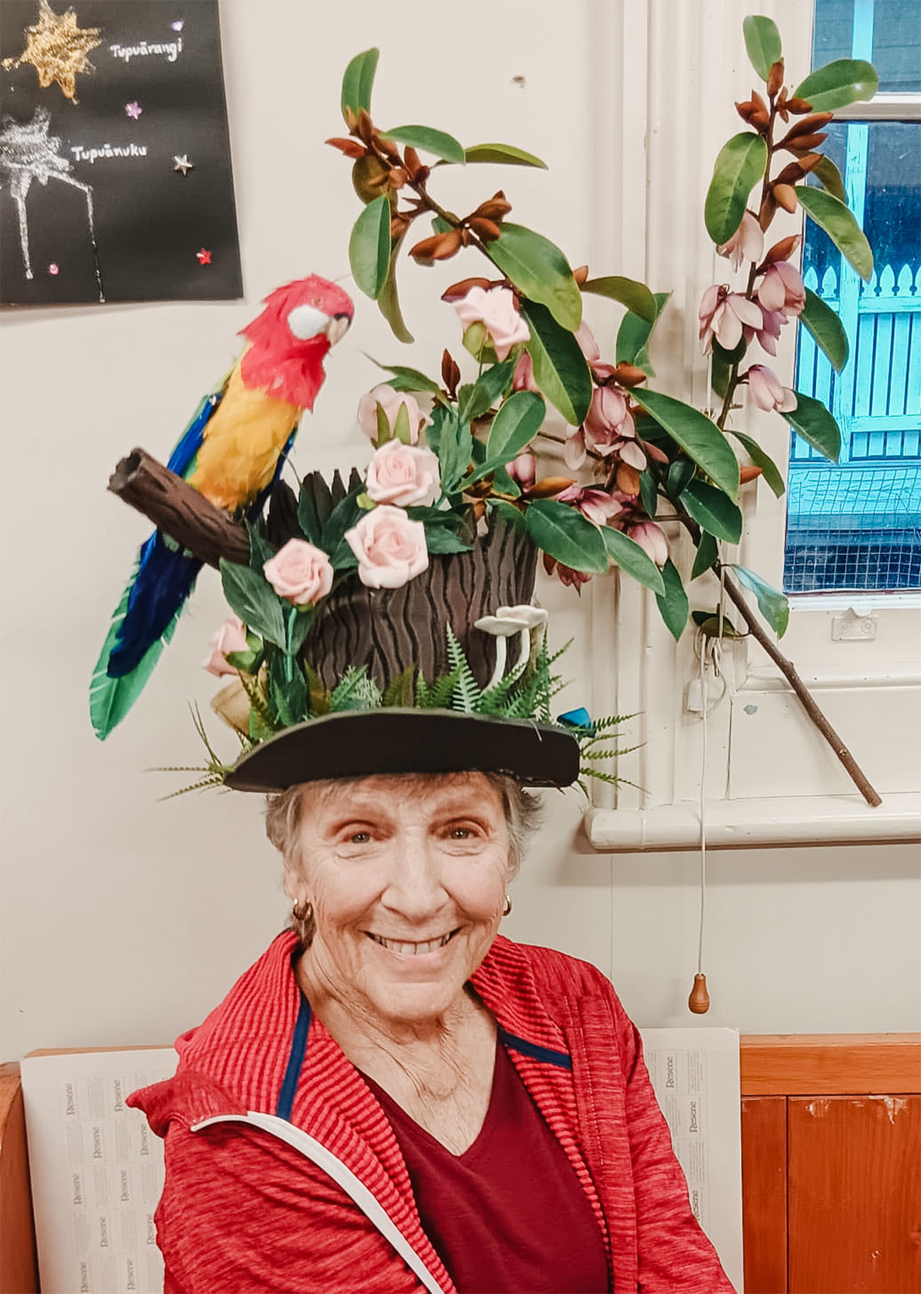 a woman wears a hat decorated with branches and a parrot
