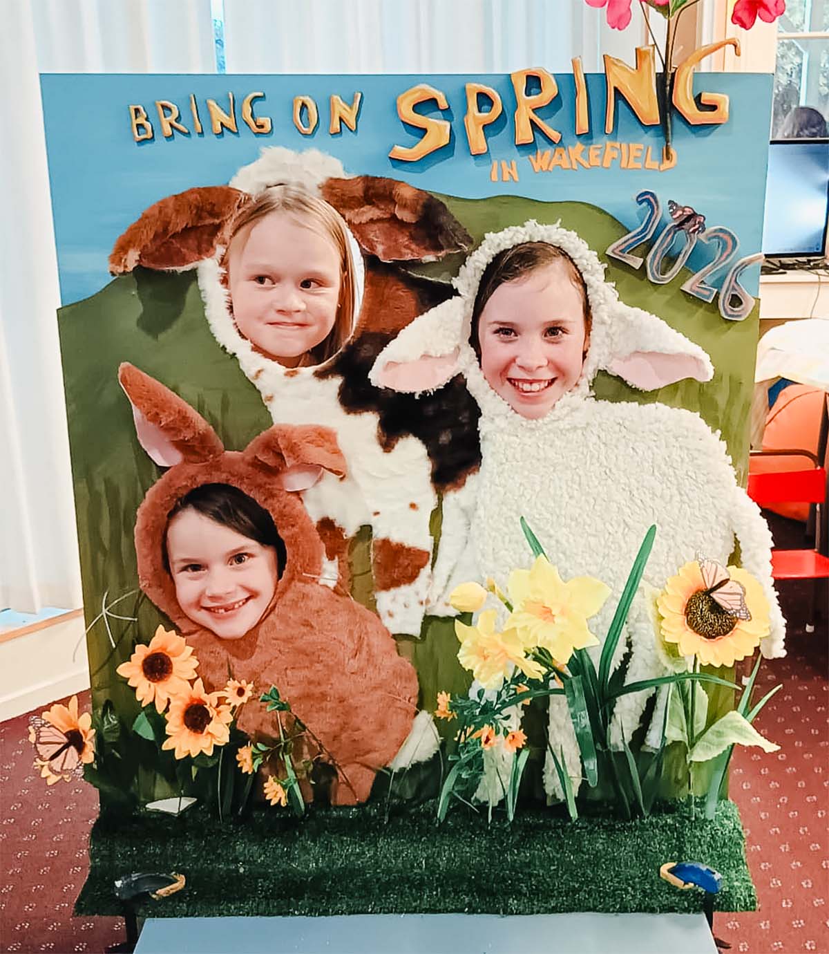 kids poke their heads through a photoboard that says "bring on spring" with farmyard animals
