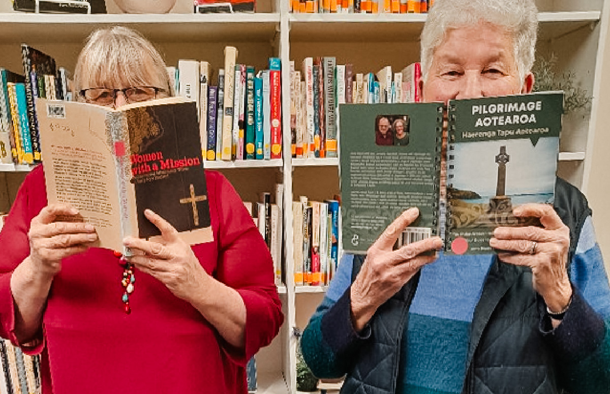 Raewyn Parkes and Miriam Taylor holding books in front of their faces with just their eyes visible
