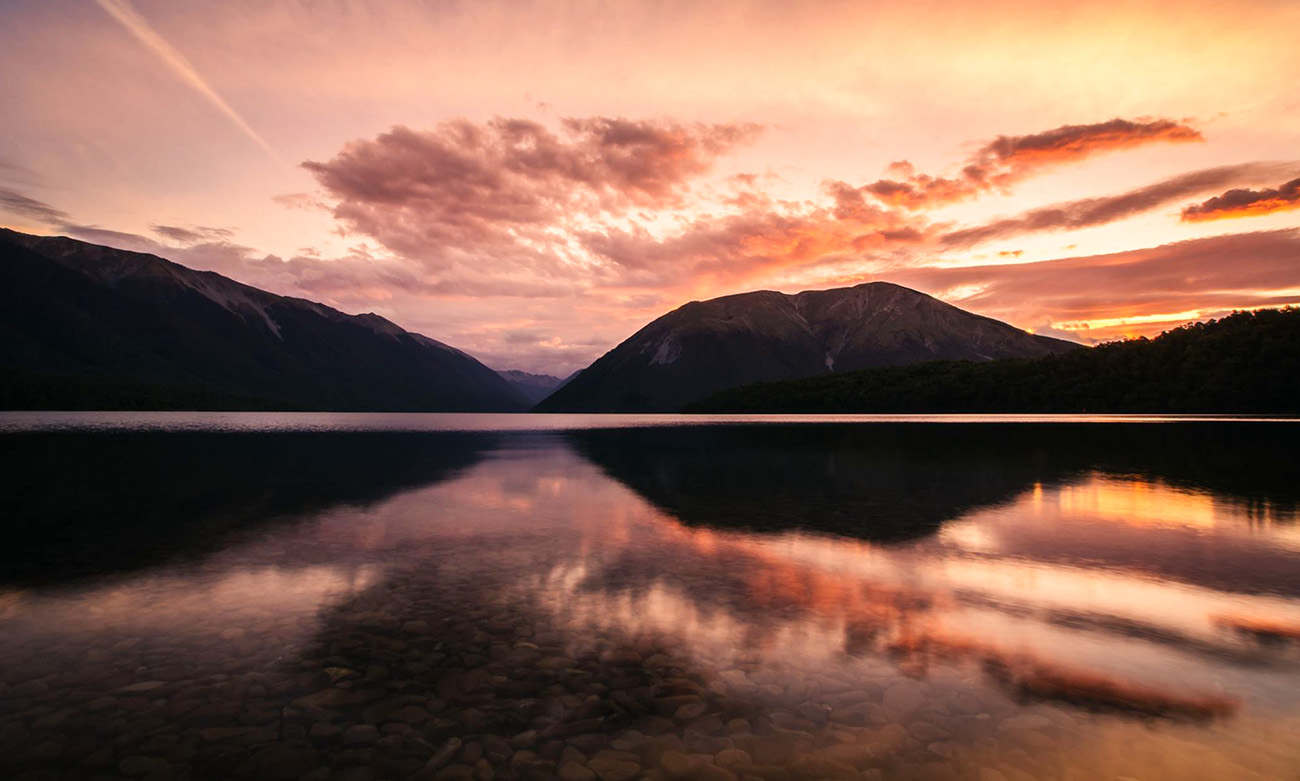 A calm lake reflecting mountains behind at sunset
