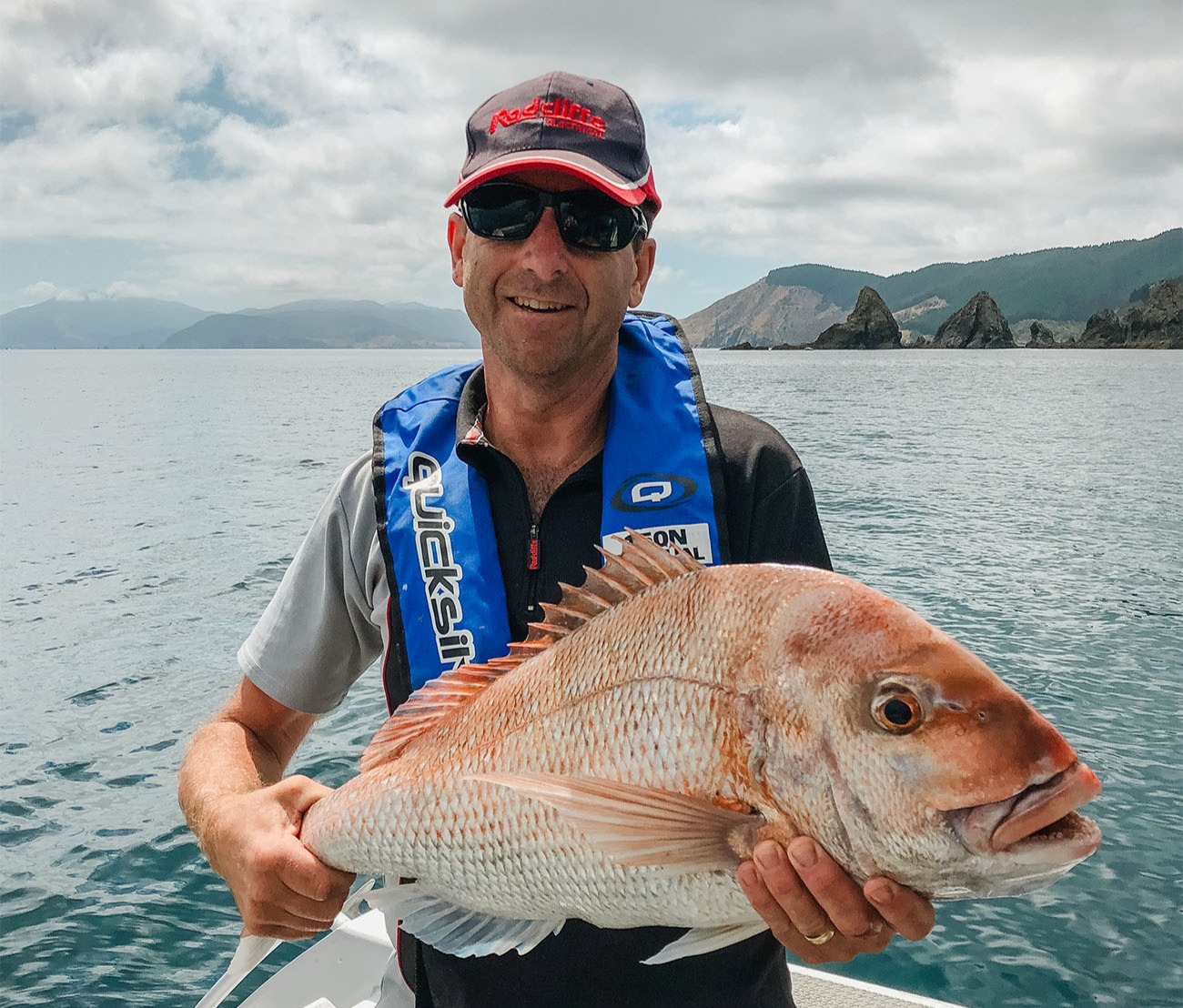 a man on a boat holding a large reddish fish