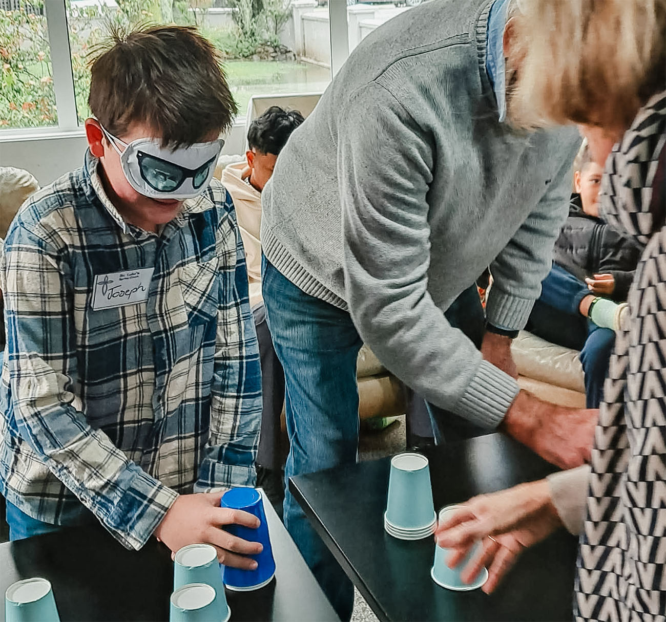 A young boy and older man stacking paper cups while blindfolded