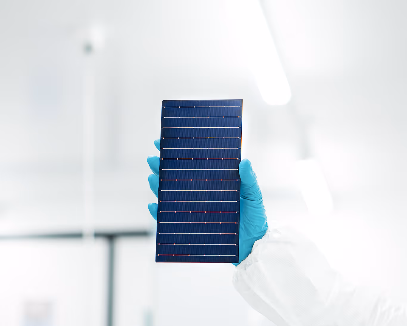 Hand wearing blue glove holding a rectangular solar panel against a bright, blurred background.