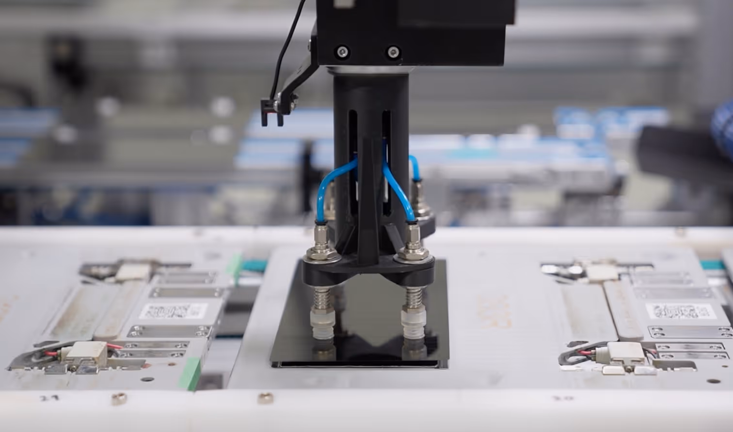 Automated robotic arm with suction cups handling a smartphone screen protector in a manufacturing setting.