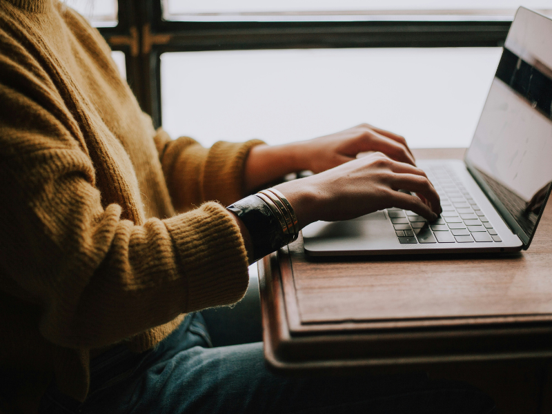 Person in yellow sweater typing into a laptop