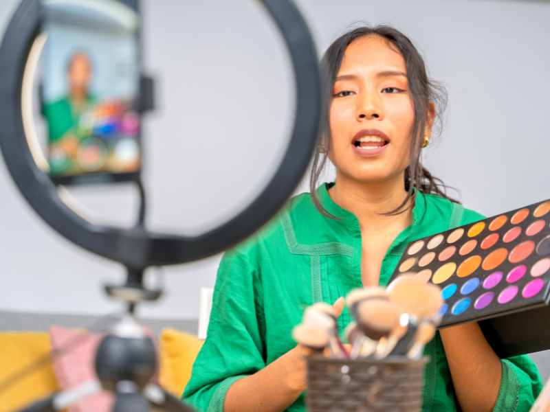 A young girl filming a make-up tutorial in front of her ring light and camera for YouTube