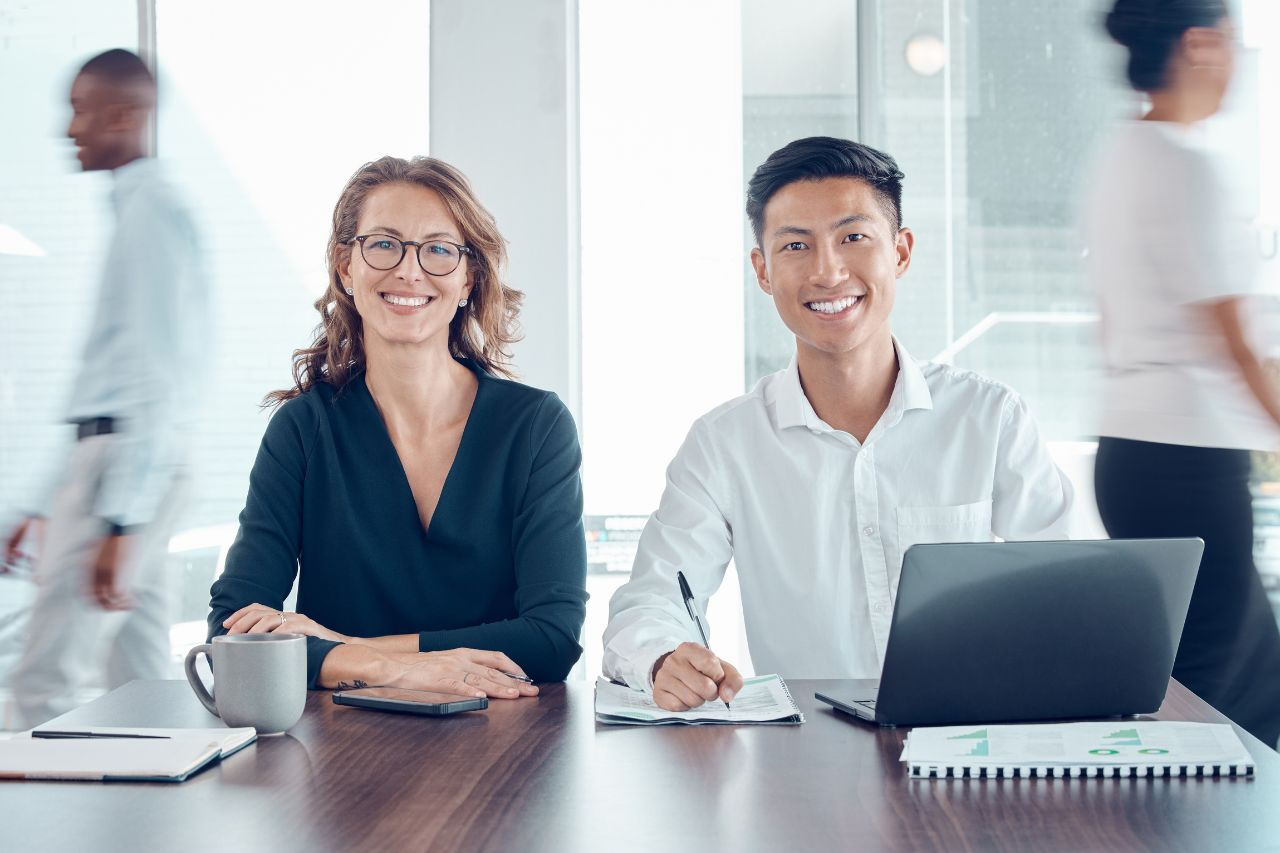 Two businesspeople sitting at a desk and smiling.