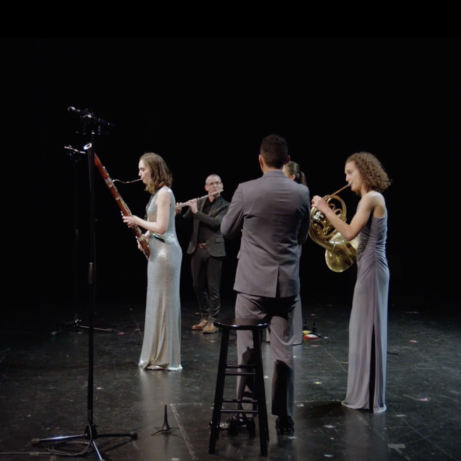 Five artists playing wind instruments and dressed formally on stage