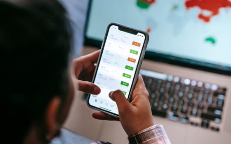 An investor checking options positions on a phone in front of a laptop