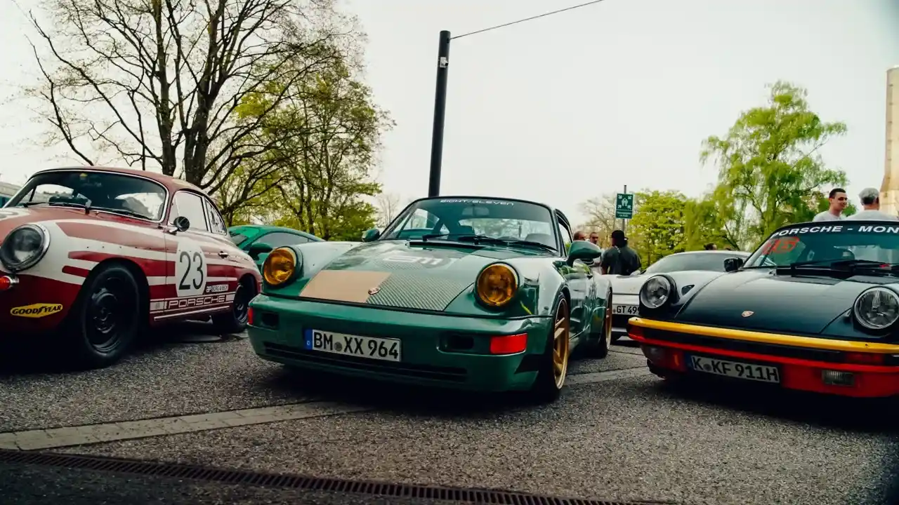 Mehrere klassische Porsche 911 stehen bei einem Treffen nebeneinander; grüner 964 vorn im Bild.