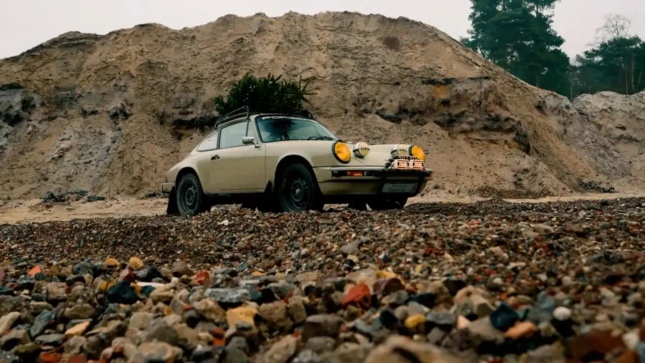 Klassischer Porsche 911 mit Dachgepäckträger und Zusatzscheinwerfern steht in einer Kiesgrube.