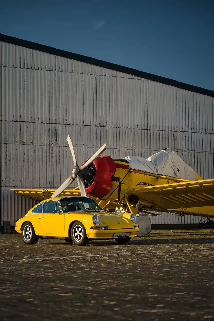 Gelber Porsche 911 parkt vor einem gelben Propellerflugzeug am Hangar.