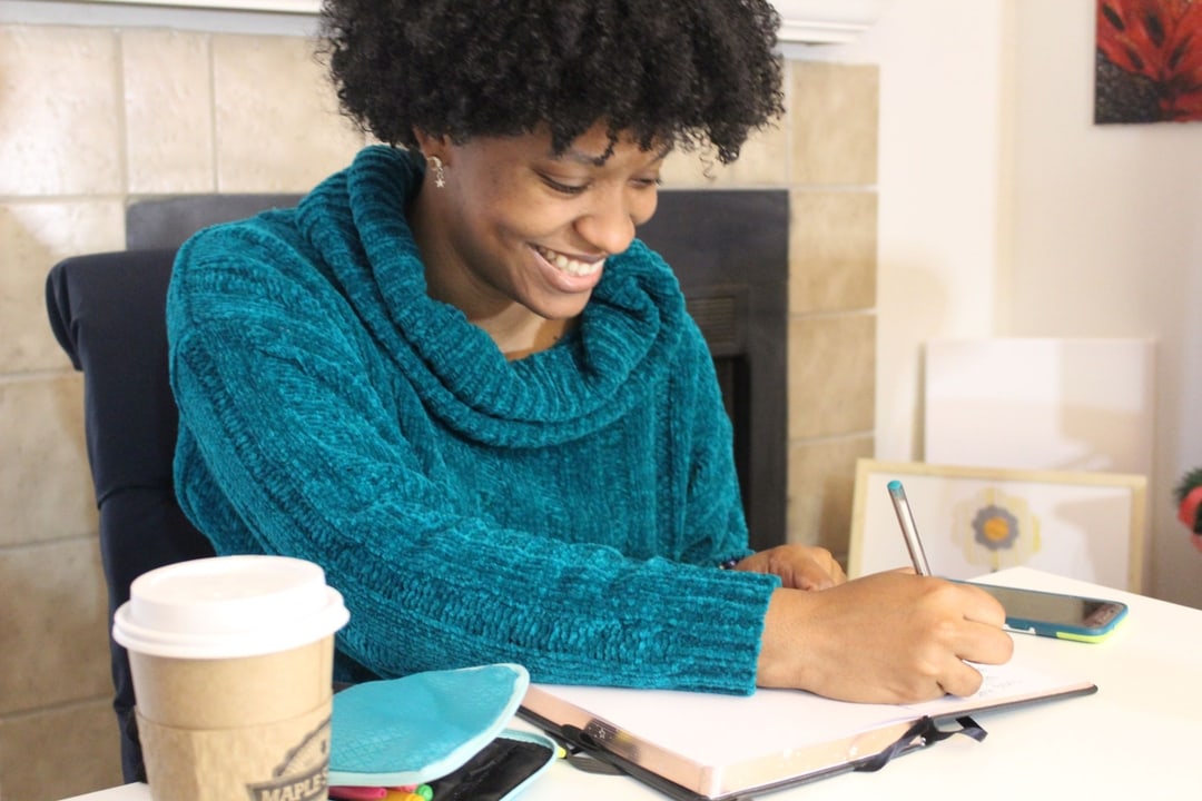 Young Woman with black curly hair happily writing in a journal