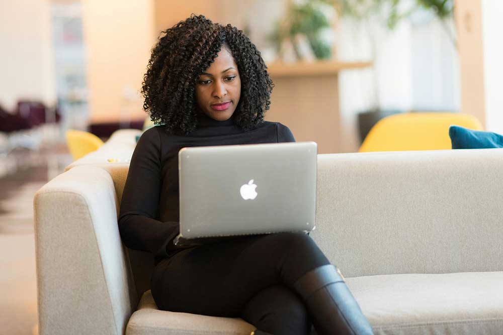 Woman works on a laptop while sitting on a couch.