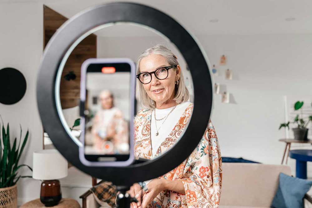 Woman looks through a ring light while recording a video of herself on her phone.