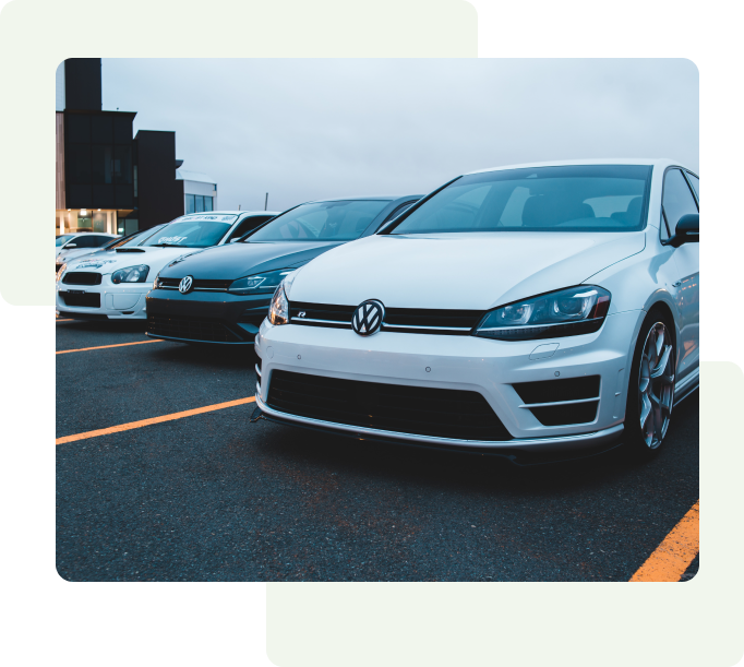 Three parked cars in a row with a white Volkswagen in front, followed by a black Volkswagen, and a white Subaru in the background.
